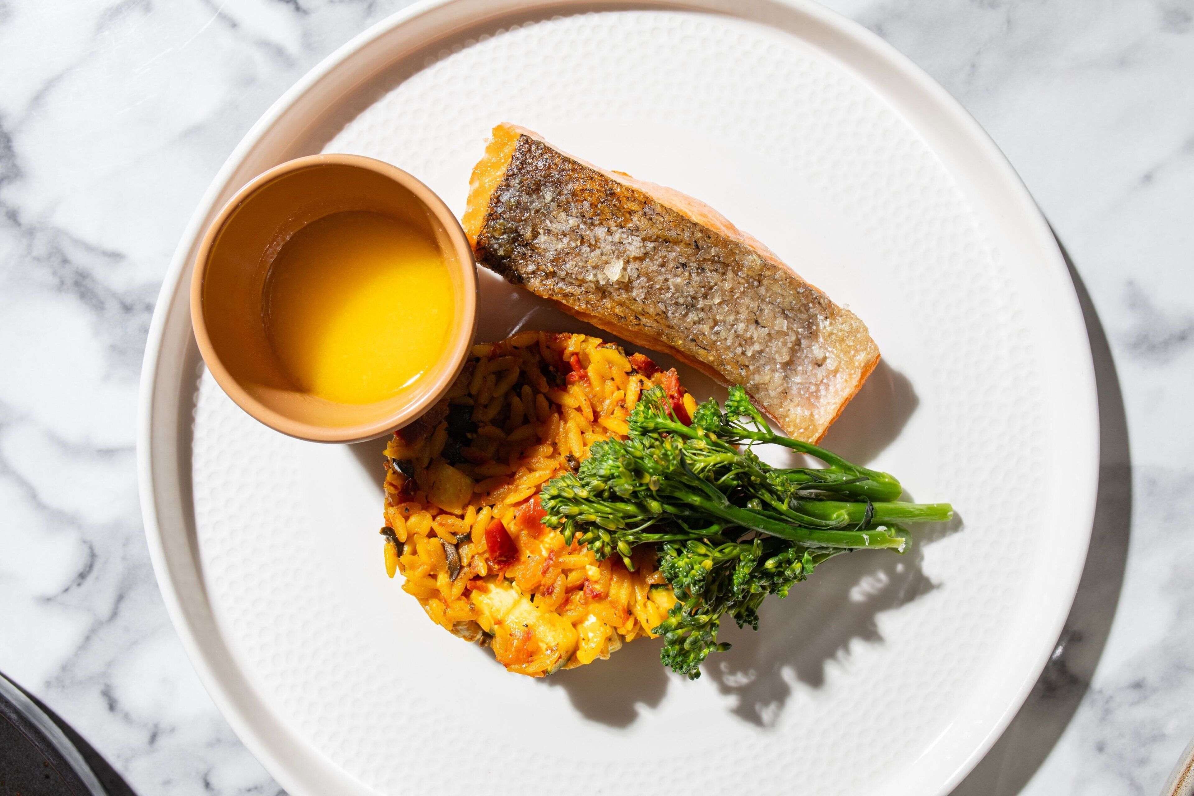 A plate with a slice of bread, a small bowl of sauce, and a serving of rice with vegetables.