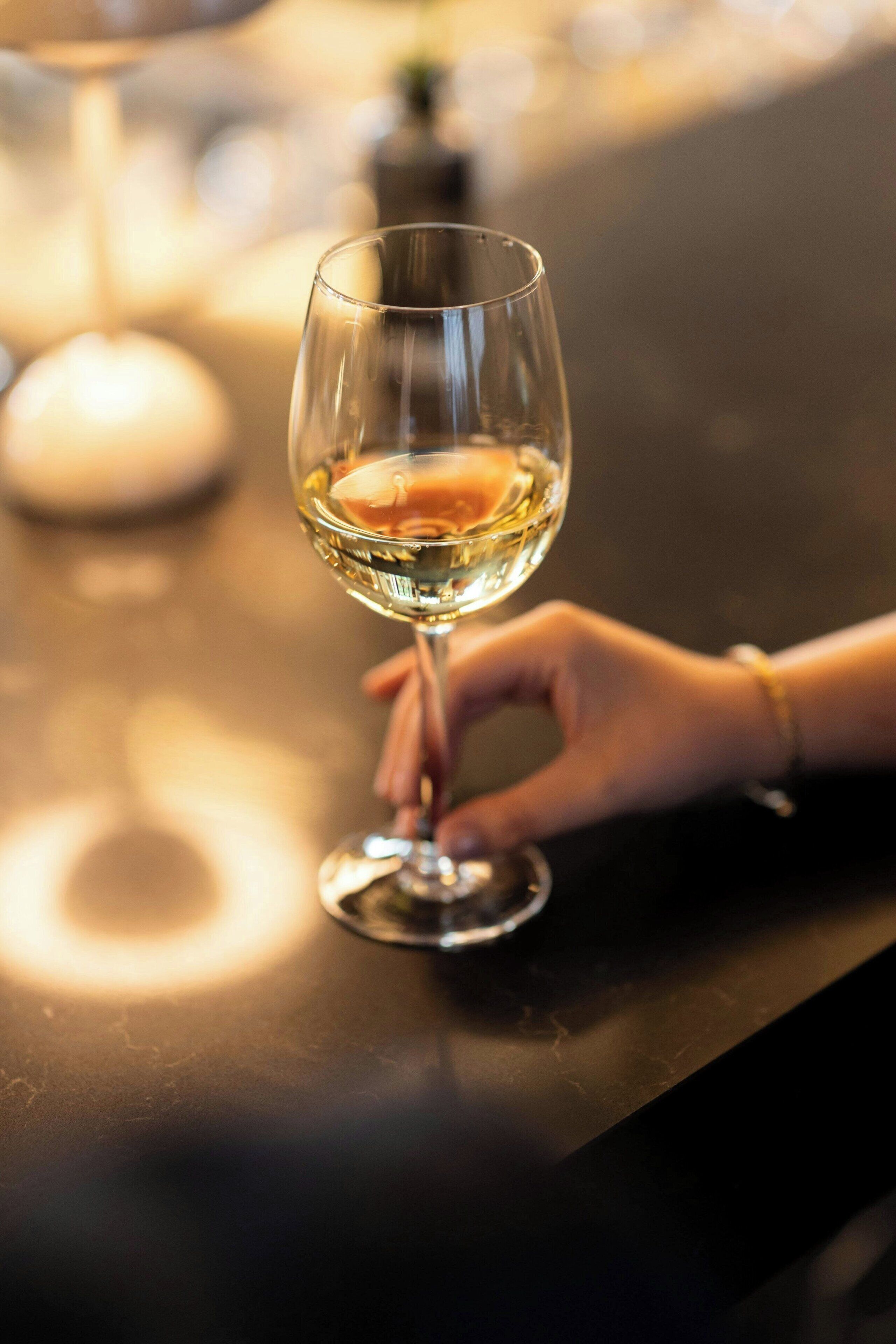 A hand holding a wine glass on a bar counter.