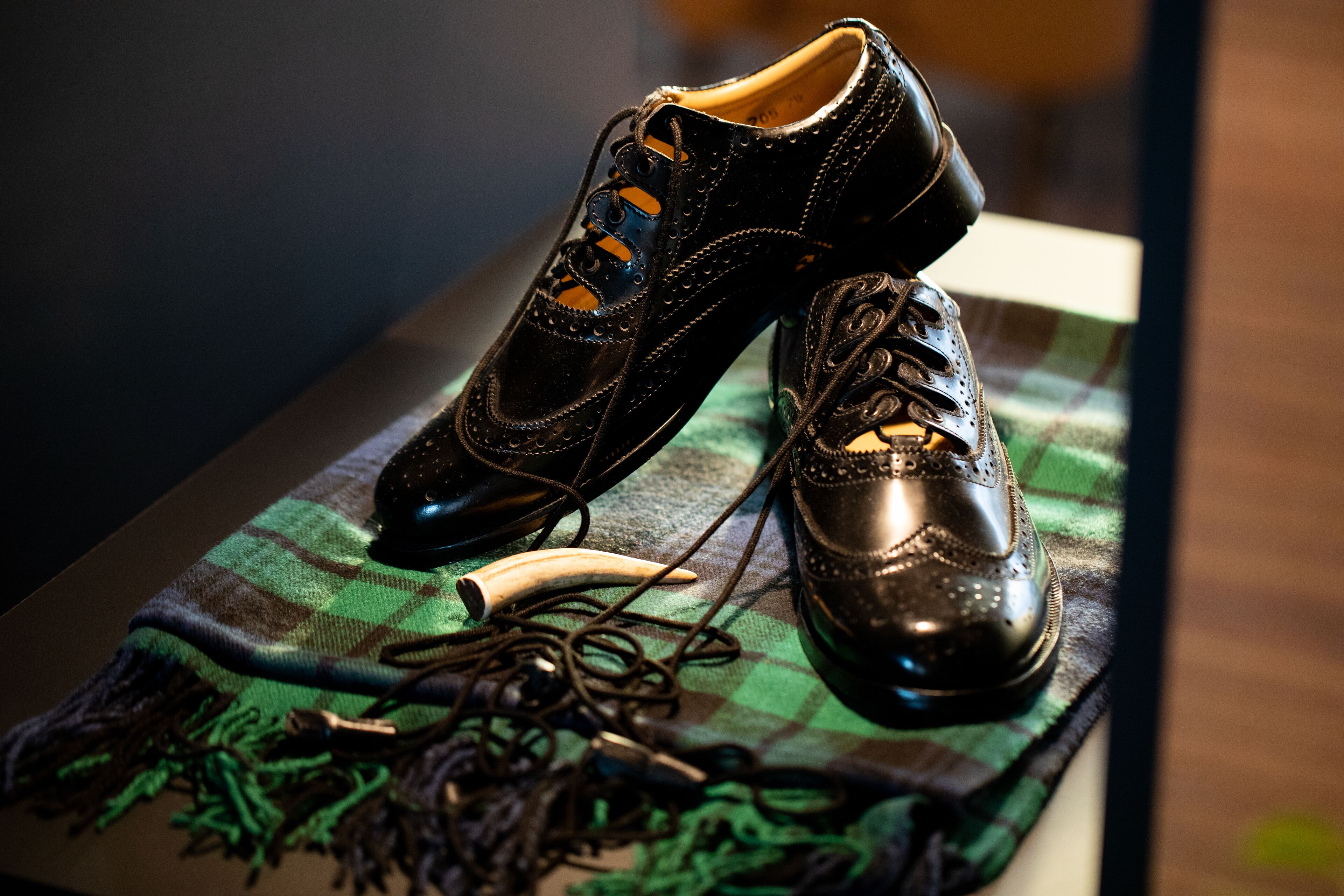 A pair of black shoes on a plaid cloth with a banana and some cords.
