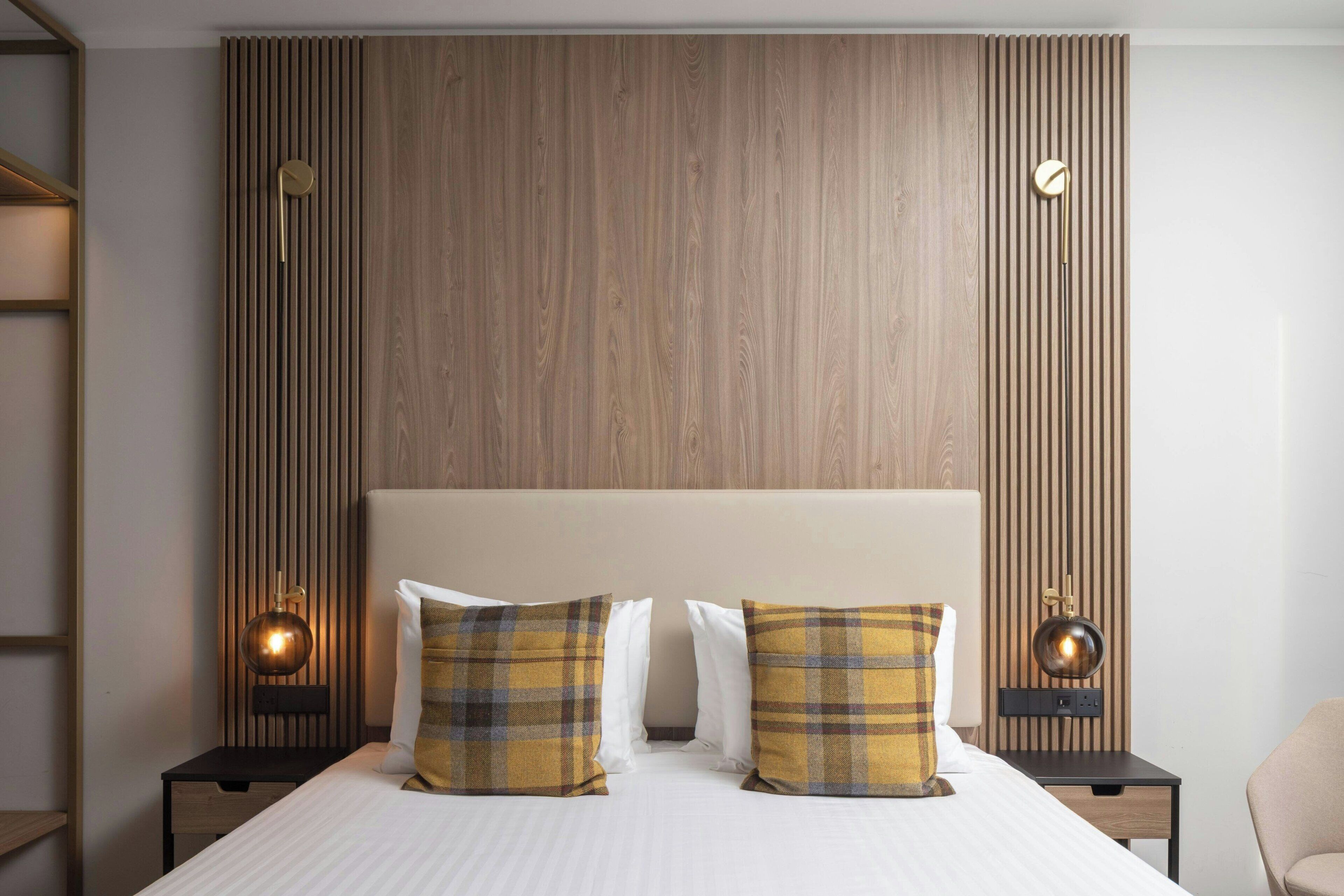 A hotel room with a large bed, two bedside tables with lamps, a wooden panel wall, and a modern design.