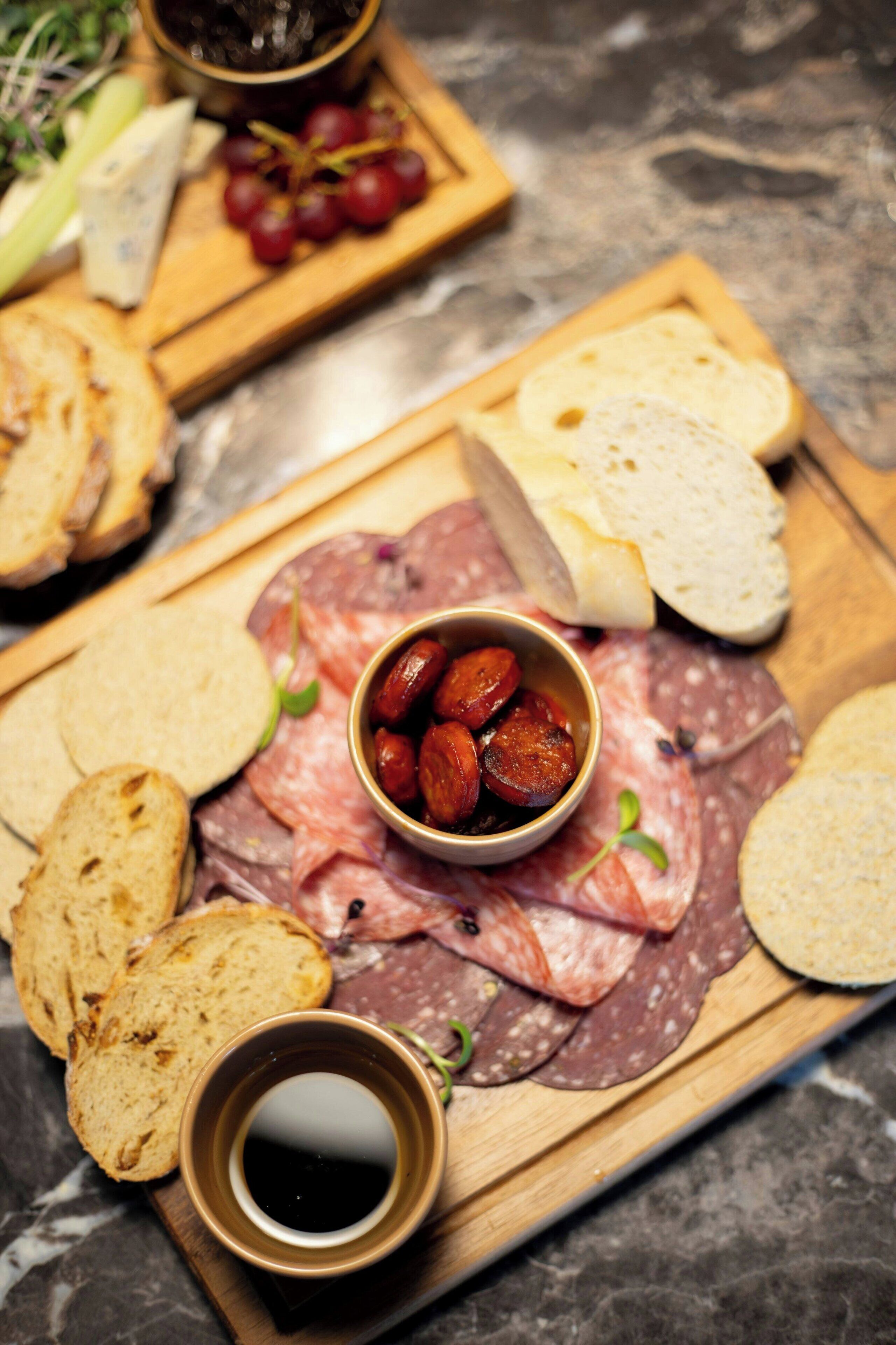 A charcuterie board with various meats, cheeses, and bread, accompanied by a bowl of olives and a cup of sauce.