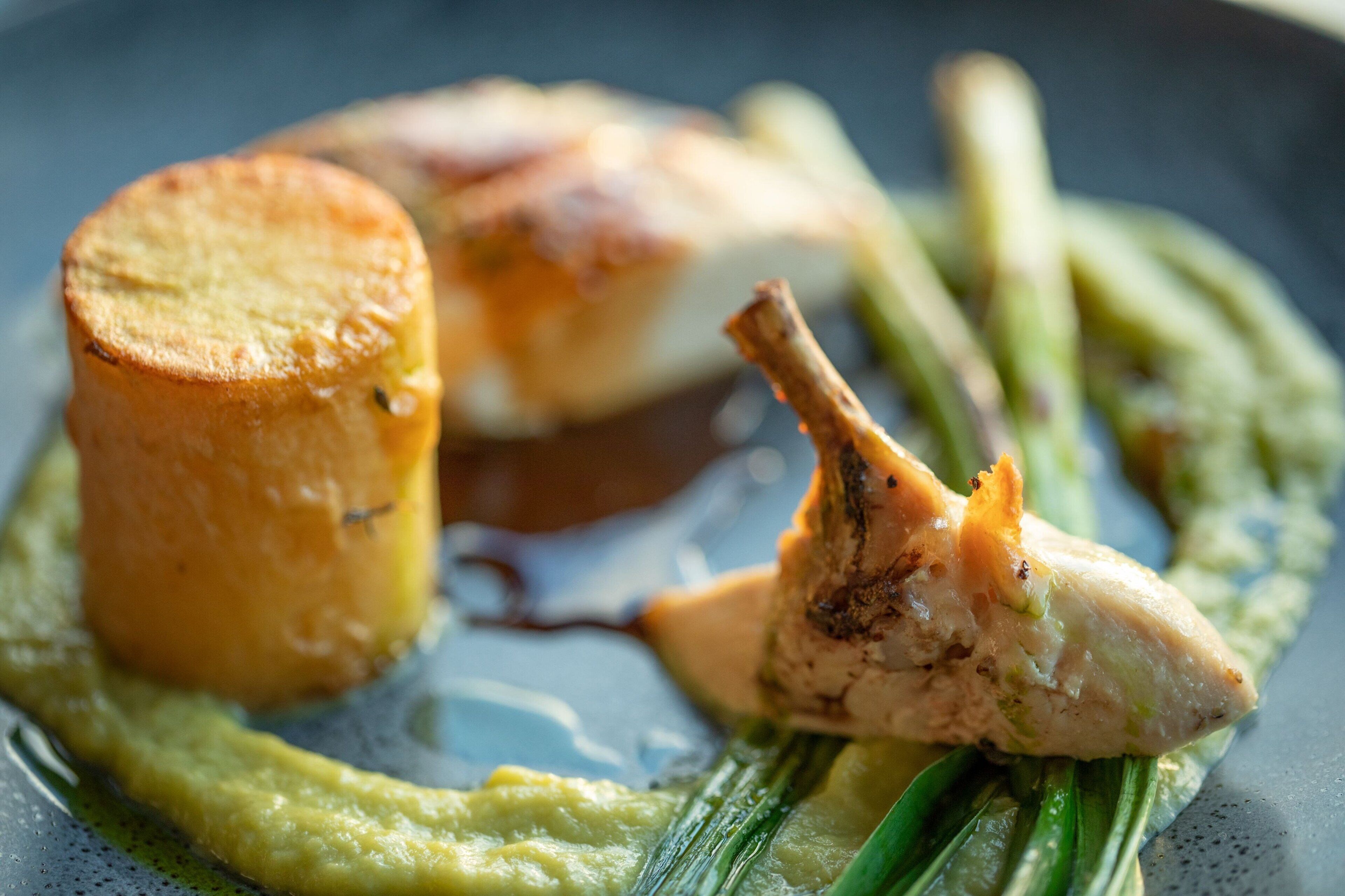 A dish with a piece of meat, a cylindrical item, and green vegetables on a plate.