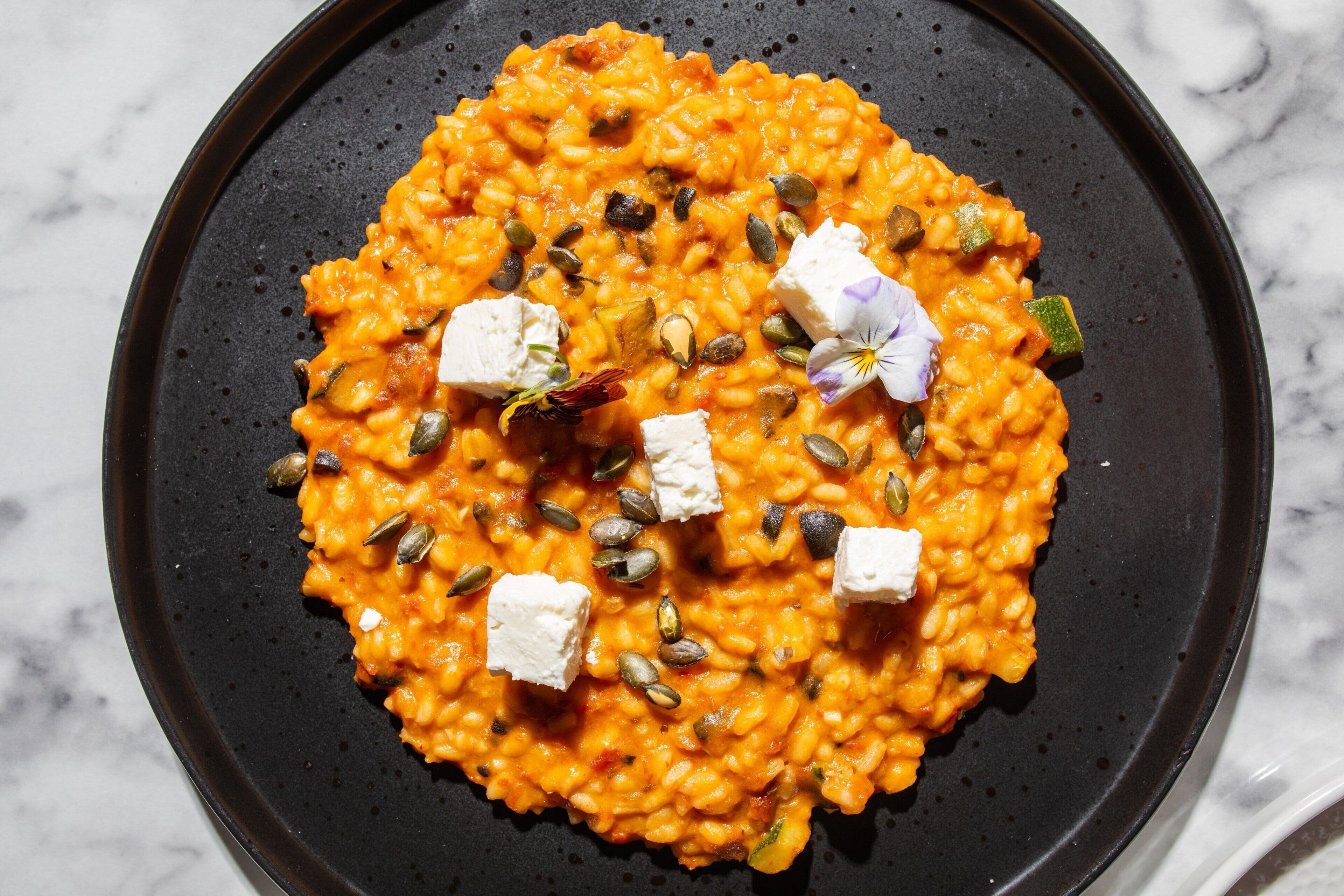 Un piatto di risotto con semi di zucca e formaggio, su un piatto nero.