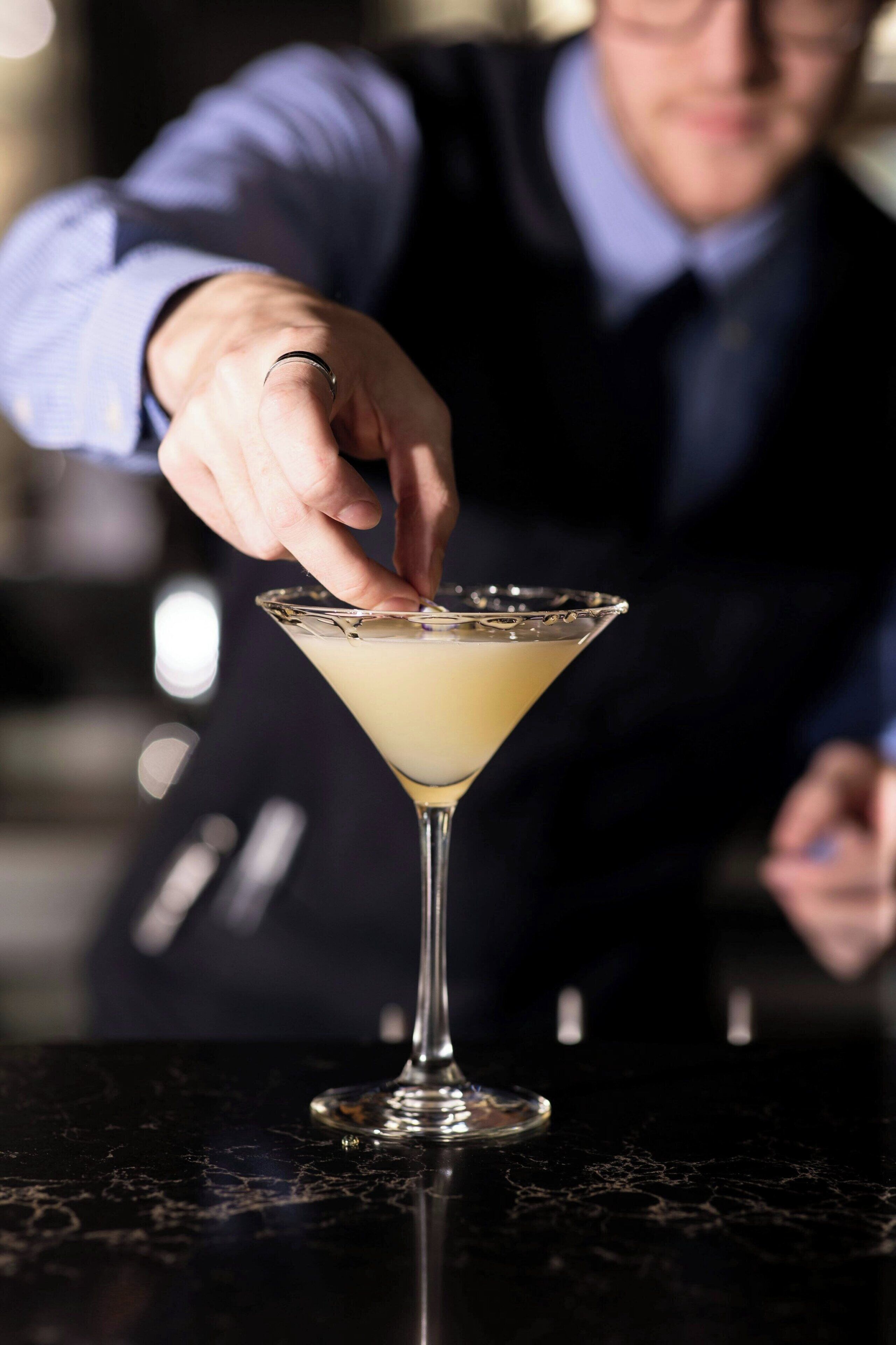 A person in a suit preparing a martini on a bar counter.