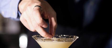 A person in a suit preparing a martini on a bar counter.