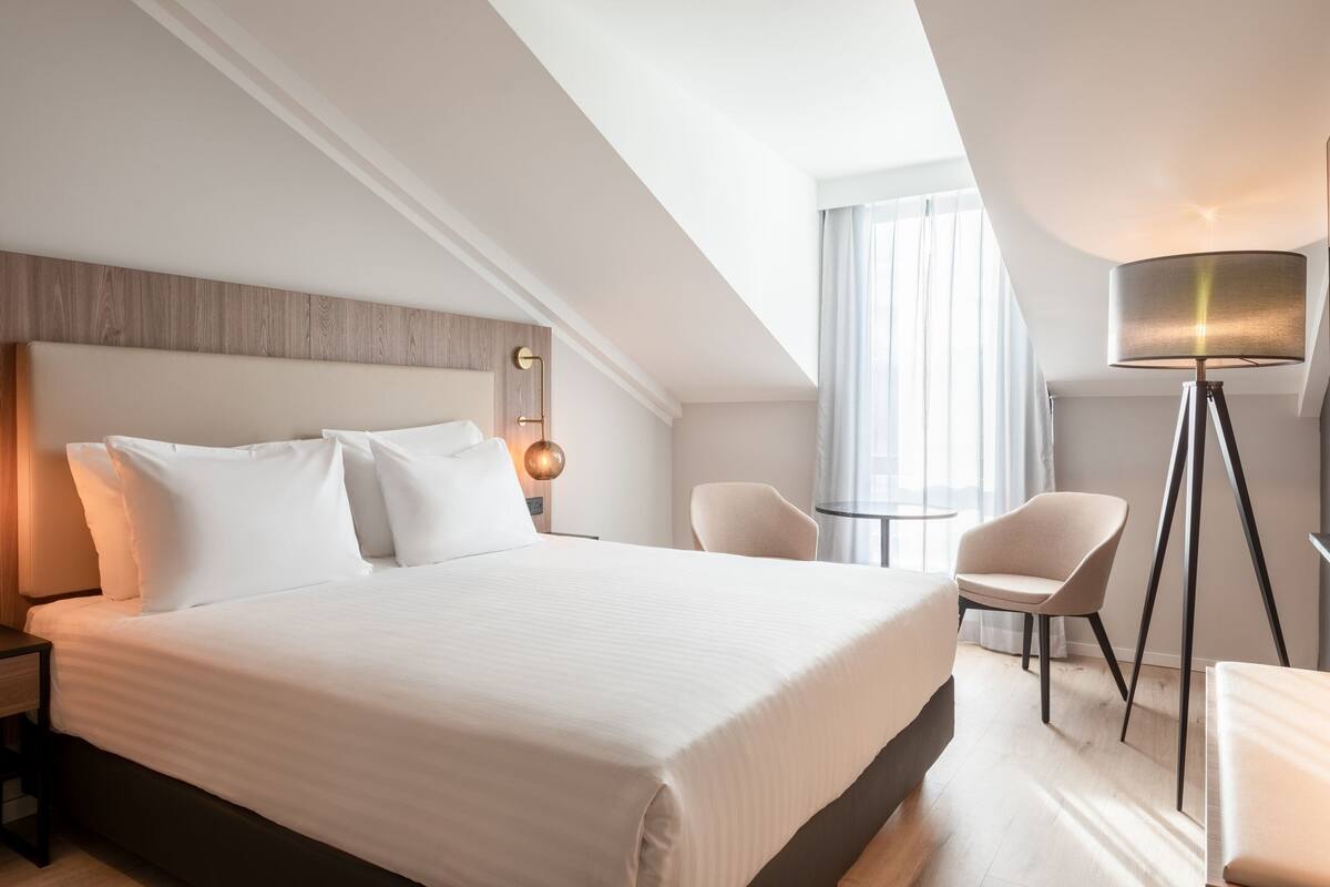 Una habitación de hotel moderna con una cama grande, un escritorio, una silla y una lámpara de pie.