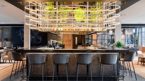 A modern bar area with a central island, multiple seating options, and a unique ceiling design with integrated greenery. - AC Hotel by Marriott Inverness (Inverness)