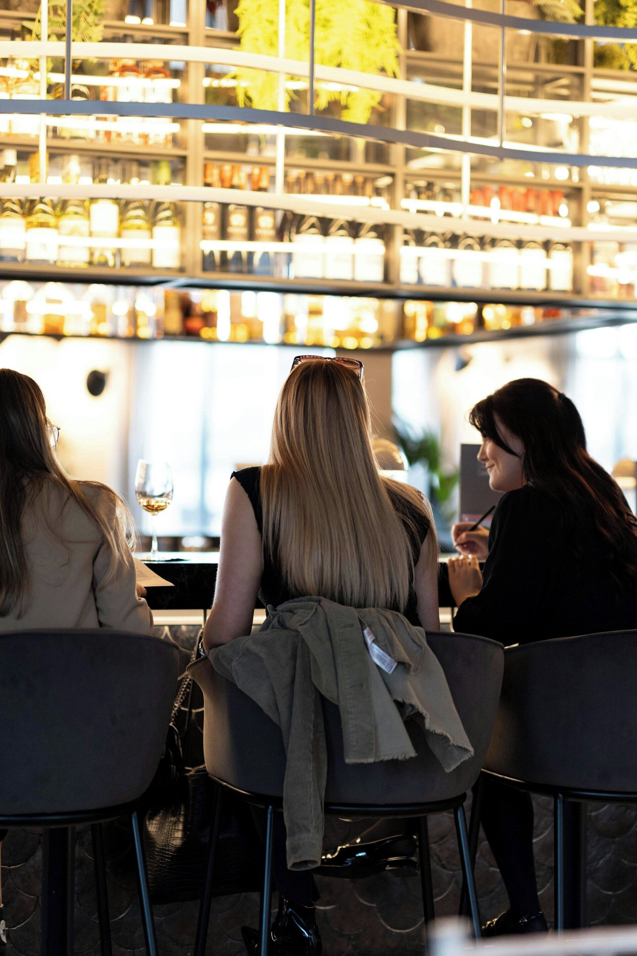 Tres personas sentadas a una mesa en un restaurante, con una barra de bar al fondo.