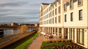 A modern building with a riverside patio area, featuring outdoor seating and a view of the water. - AC Hotel by Marriott Inverness (Inverness)