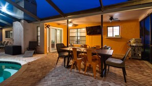 Un patio exterior con piscina, zona de comedor con sillas y mesa, y una parrilla.