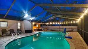 Una piscina interior con techo de cristal, sillas junto a la piscina y una zona de estar hundida.