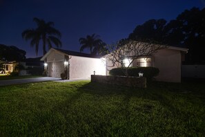Uma casa residencial à noite, com uma entrada iluminada e gramado.