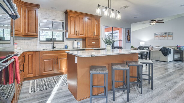 Una cocina moderna con armarios de madera, una isla grande con taburetes y un comedor con ventilador de techo.