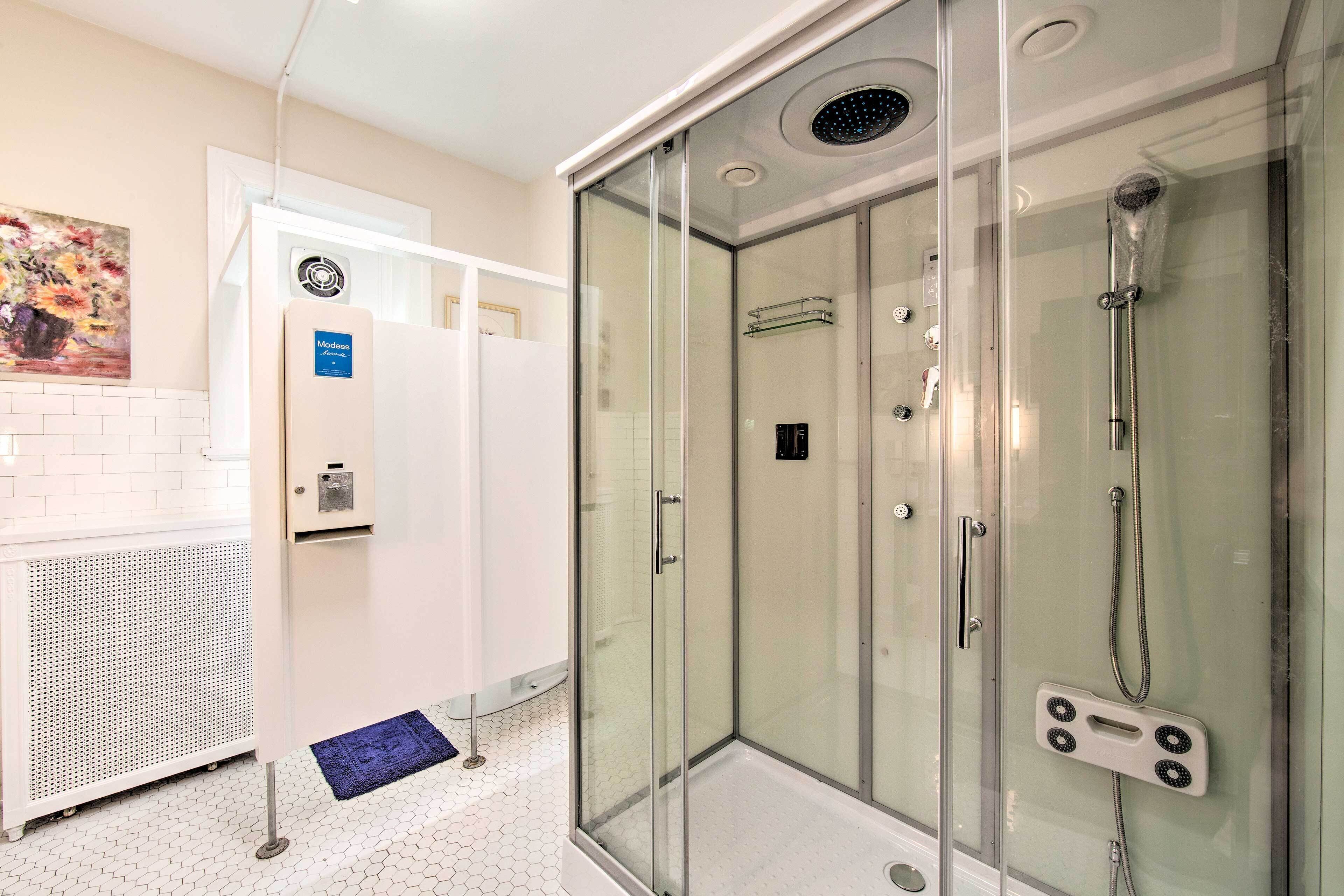 Une salle de bain moderne avec une douche en verre, un sol carrelé de couleur blanche et un chauffe-eau apparent.