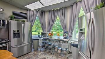 A modern kitchen with stainless steel appliances, a large window with curtains, and a cart with pots and pans.