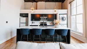 A modern kitchen with a central island, bar stools, a built-in oven, and a washing machine. - Tailor Loft Studio| Living in the Heart of Knox (Knoxville)