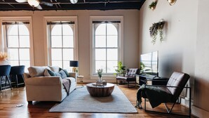 A spacious living room with a large window, a ceiling fan, and a leather armchair. - Tailor Loft Studio| Living in the Heart of Knox (Knoxville)