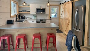 A modern kitchen with wooden cabinets, stainless steel appliances, and red bar stools. - Perfect 4-season cottage for year-round joy (Whitestone)