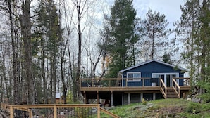 A wooden dock leading to a house with a blue exterior and a wooden deck. - Perfect 4-season cottage for year-round joy (Whitestone)