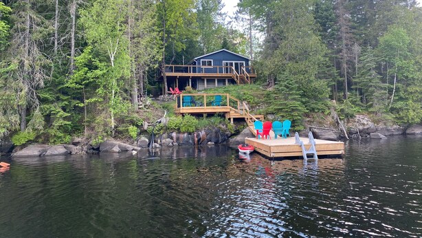 A cabin with a dock and a small boat, surrounded by dense forest. - Perfect 4-season cottage for year-round joy (Whitestone)