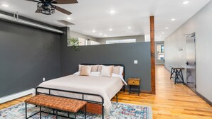 Un dormitorio moderno con cama, banco, ventilador de techo y una mesita.