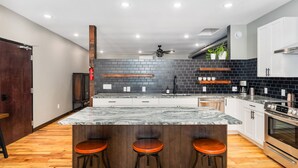 Una cocina moderna con una isla de mármol, taburetes de madera y un salpicadero de ladrillo negro.