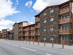 Une rangée d’immeubles à étages avec des balcons, un ciel dégagé et une route au premier plan.