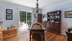 A spacious dining area with a wooden table and chairs, a chandelier, and a view of the outdoors through a glass door. - Pool Property in West Cape May - Sleeps 6 Guests (West Cape May)