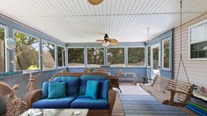 A covered porch with a blue sofa, wicker furniture, and a hanging swing. - Pool Property in West Cape May - Sleeps 6 Guests (West Cape May)