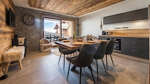 A modern kitchen with dark cabinets, a wooden ceiling, and a dining area with a table and chairs. - Olvera 502 - New apartment on the slopes (VALMEINIER)