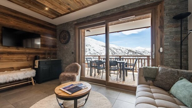 A cozy living room with a fireplace, a sofa, a chair, and a dining area with a view of snow-covered mountains. - Olvera 502 - New apartment on the slopes (VALMEINIER)