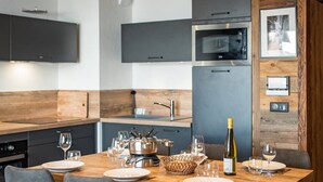A modern kitchen with a wooden dining table set for six, equipped with a microwave, oven, and a wine bottle. - Olvera 502 - New apartment on the slopes (VALMEINIER)