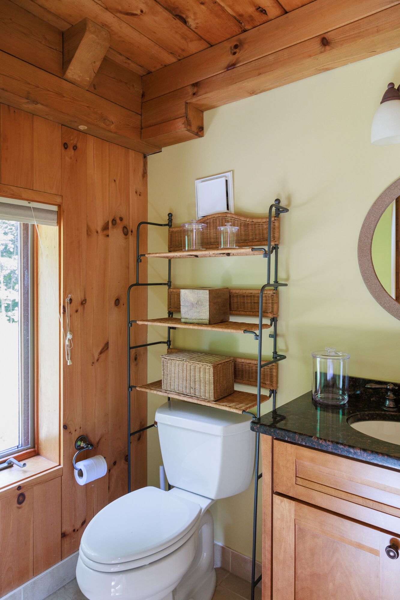 Une salle de bain en bois avec des toilettes, des étagères avec des paniers, un miroir et une fenêtre.