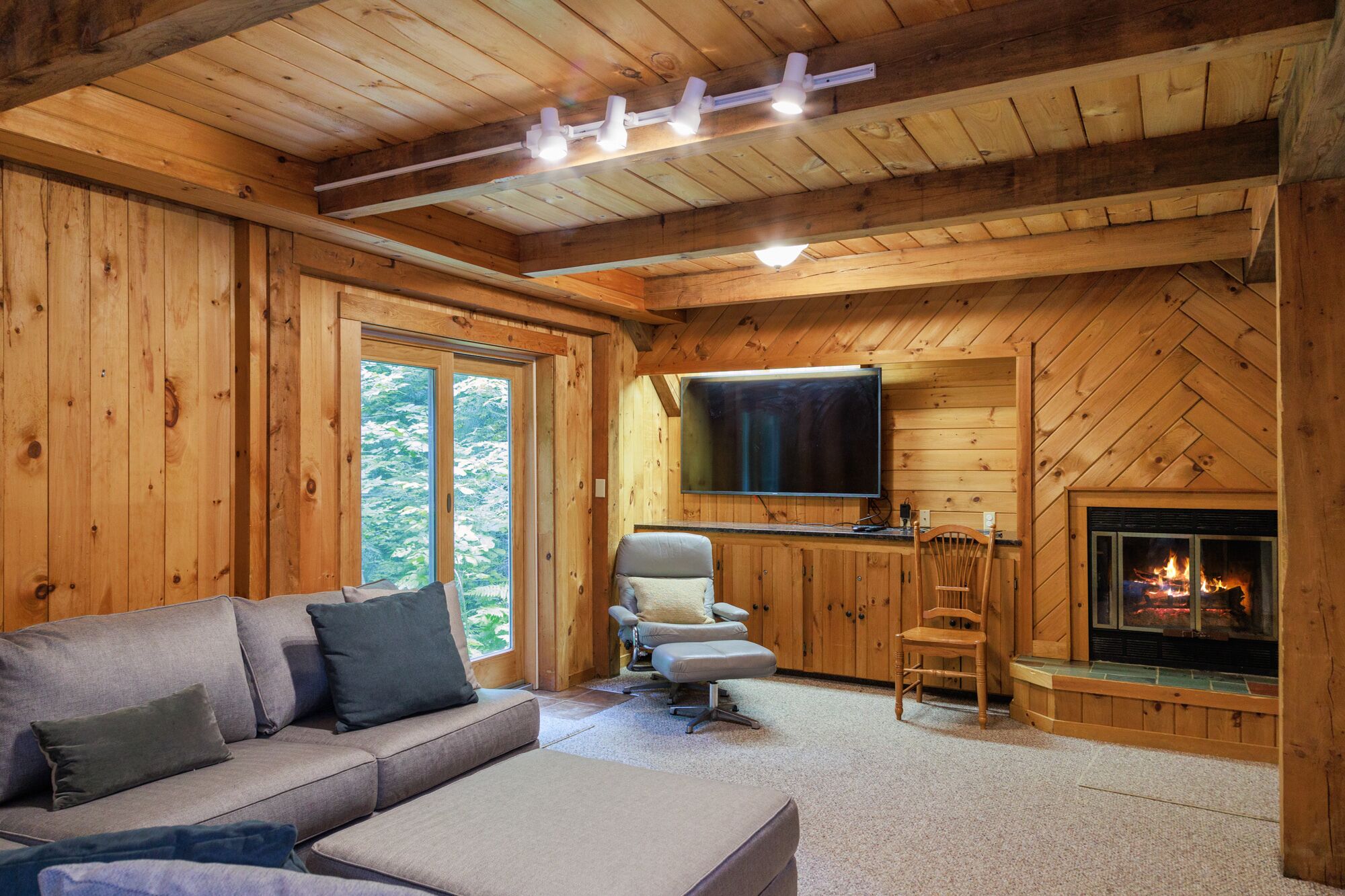 A cozy cabin interior with a wooden interior, a sofa, a chair, a flat-screen TV, and a fireplace.