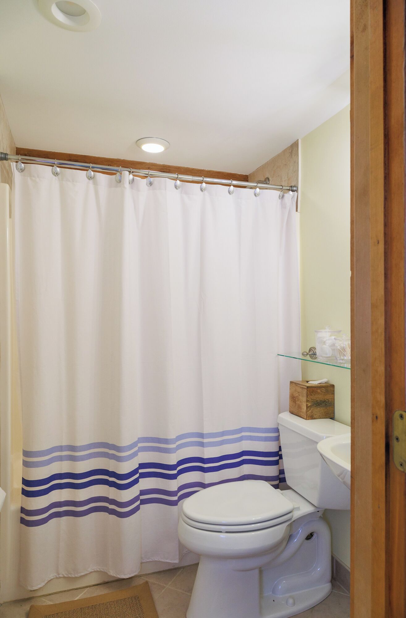 A bathroom with a white shower curtain, a toilet, and a glass shelf with toiletries.