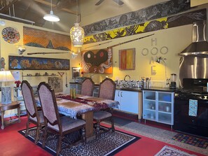 A dining area with a table and chairs, a kitchen with a stove and sink, and various wall decorations.