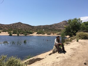 Un homme est assis sur un rocher au bord d’un lac, avec des montagnes en arrière-plan.