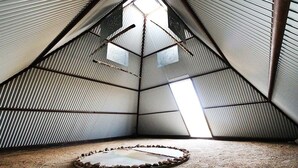 Ein dreieckiges Dachzimmer mit wellenförmigen Metallwänden, einem Oberlicht und einem kreisförmigen Steinmuster auf dem Boden.