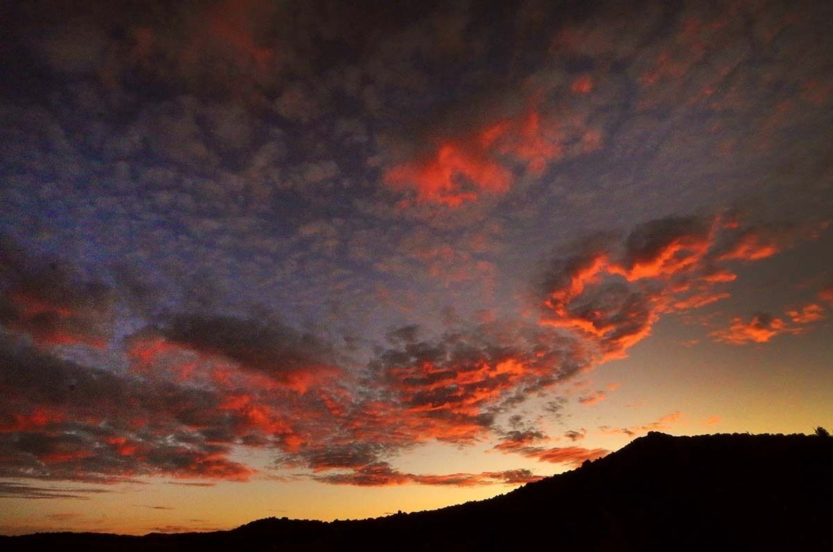 Atardecer con la silueta de una montaña y un cielo con nubes dispersas.