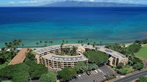 An aerial view of a circular building with a parking lot and solar panels, surrounded by palm trees and a beach. - Perfect Romantic Getaway - Right on the Ocean! (Lahaina)