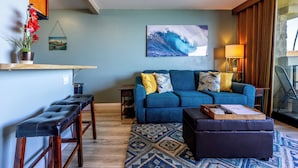 A living room with a blue sofa, a coffee table, a bench, a patterned rug, a wall-mounted TV, and a potted plant. - Perfect Romantic Getaway - Right on the Ocean! (Lahaina)