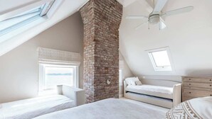 Une chambre avec une cheminée en briques, un lit, une fenêtre et un ventilateur de plafond.