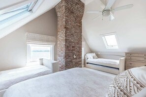 A bedroom with a brick chimney, a bed, a window, and a ceiling fan. - Beach Haven by STAY Newport (Middletown)