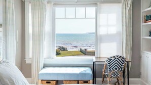 A room with a large window overlooking the sea, a bed, a chair, and a small table. - Beach Haven by STAY Newport (Middletown)
