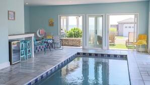 A swimming pool with a tiled deck, a bar area with stools, and a view of the outdoors. - Beach Haven by STAY Newport (Middletown)