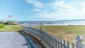 Une vue sur la côte, avec une clôture blanche en bois, un drapeau et un chemin pavé menant à la plage.
