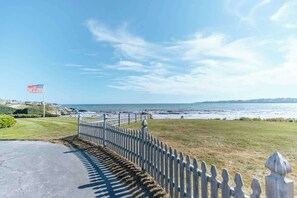 A coastal view with a white picket fence, a flag, and a paved path leading to the beach. - Beach Haven by STAY Newport (Middletown)