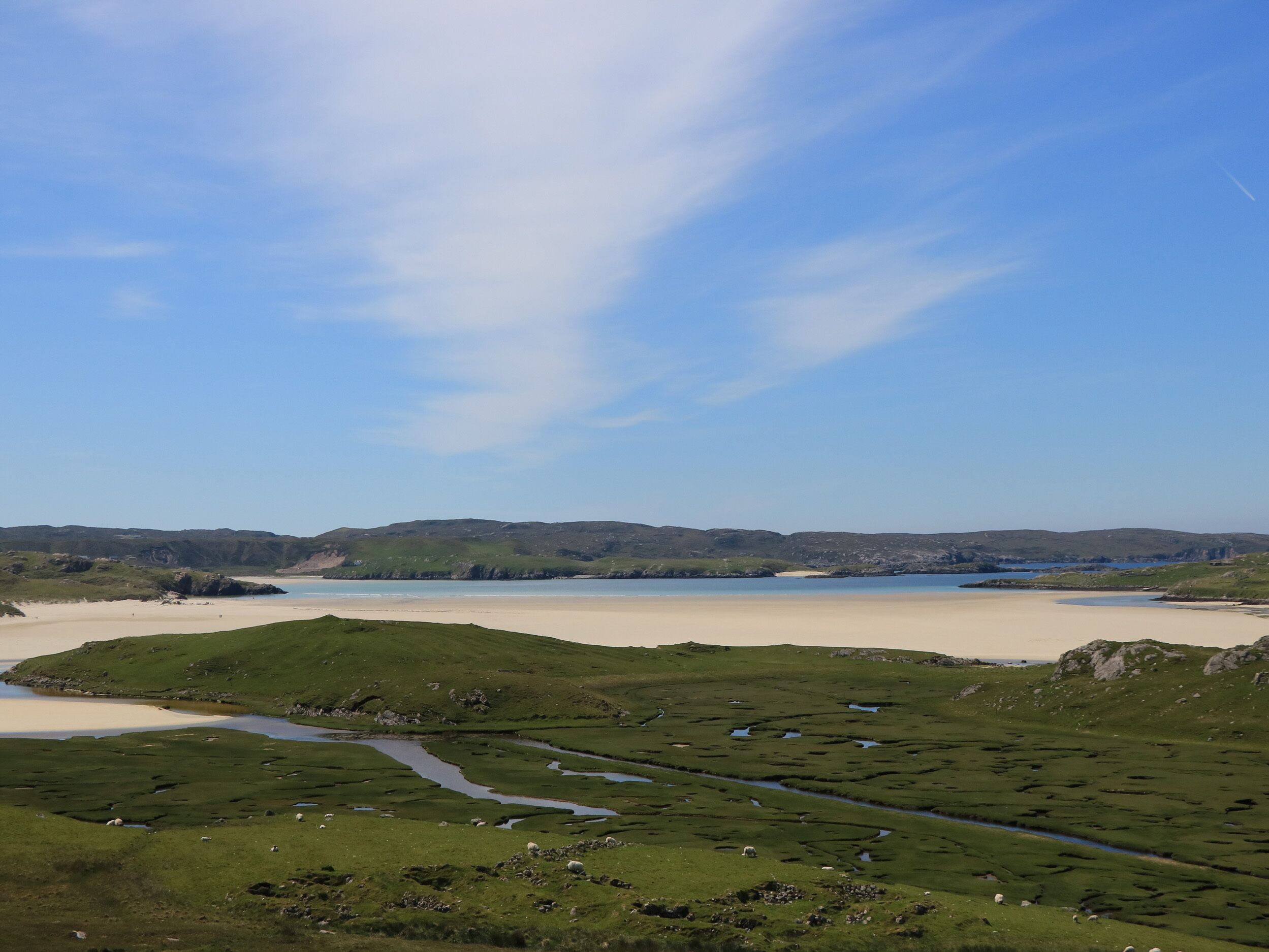 Un paysage côtier avec des champs verdoyants, une plage de sable et une étendue d’eau.