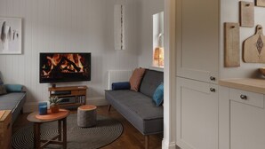 Un salon avec un téléviseur diffusant une image de cheminée, un canapé, une table basse et une petite table d’appoint.