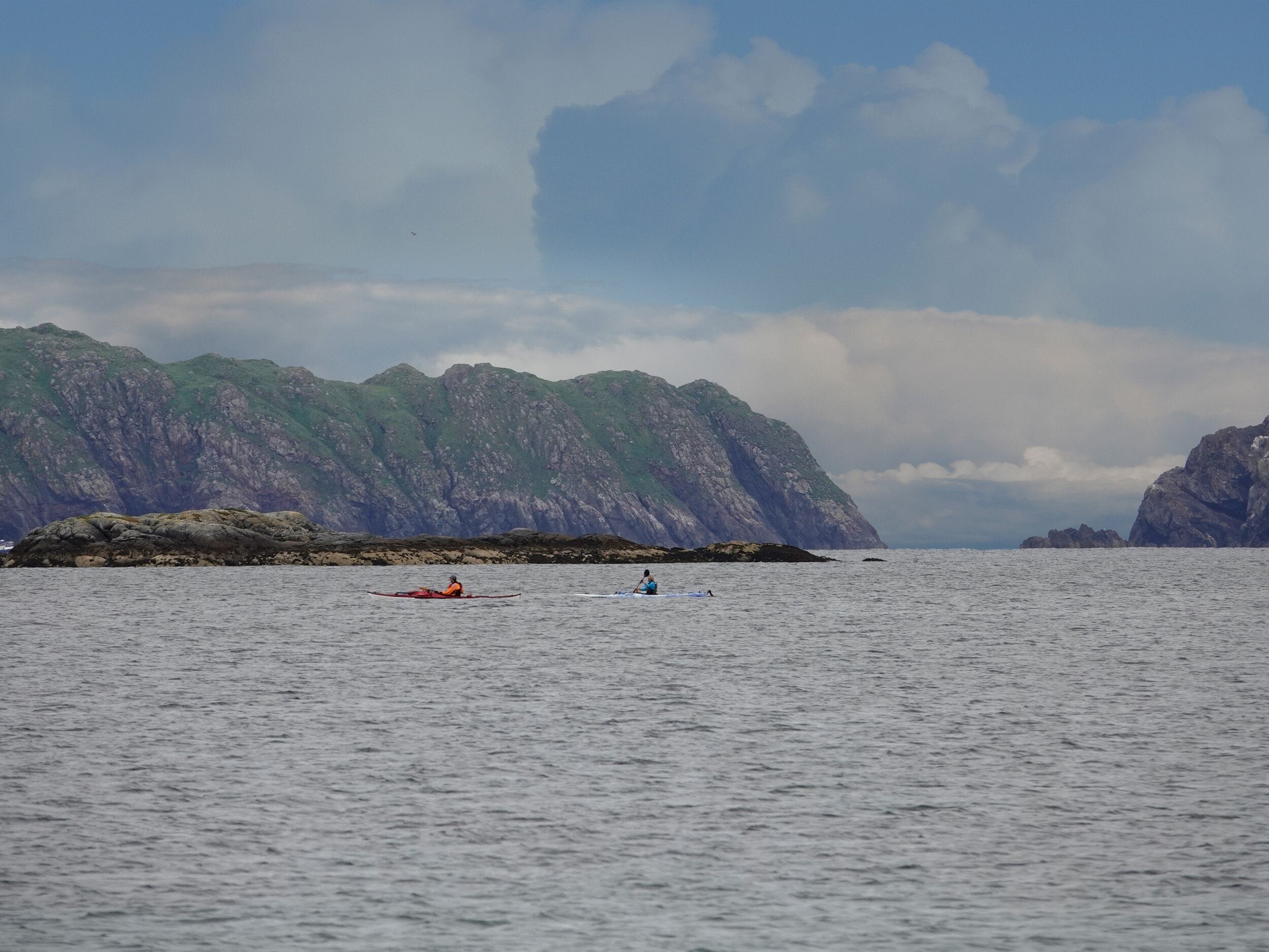 A calm sea with kayaks and a mountainous coastline.